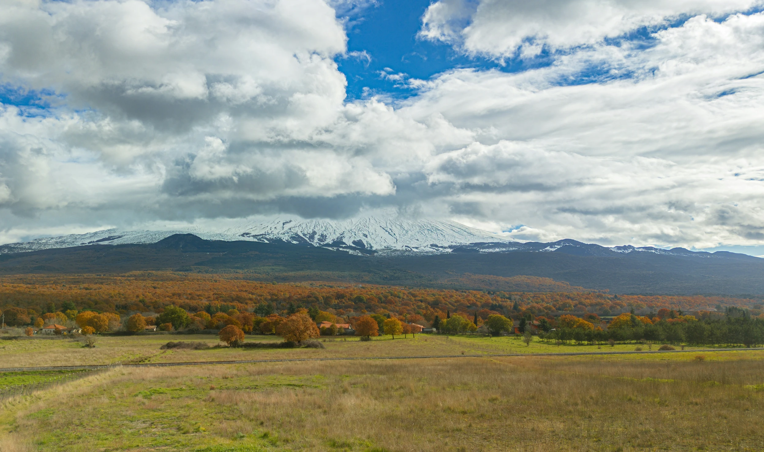 the mountain has snow on it near an open field