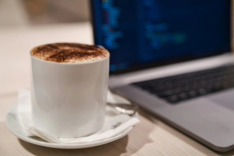 coffee cup sitting on a saucer next to a laptop computer