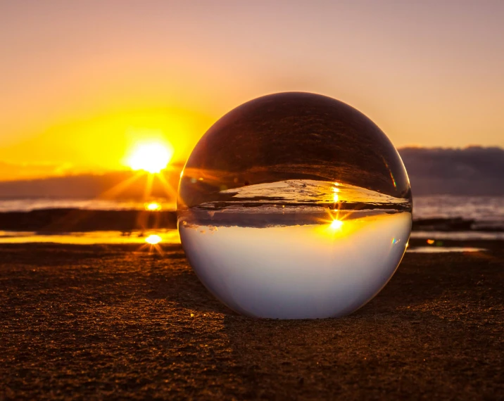 large clear sphere on sandy beach in front of setting sun