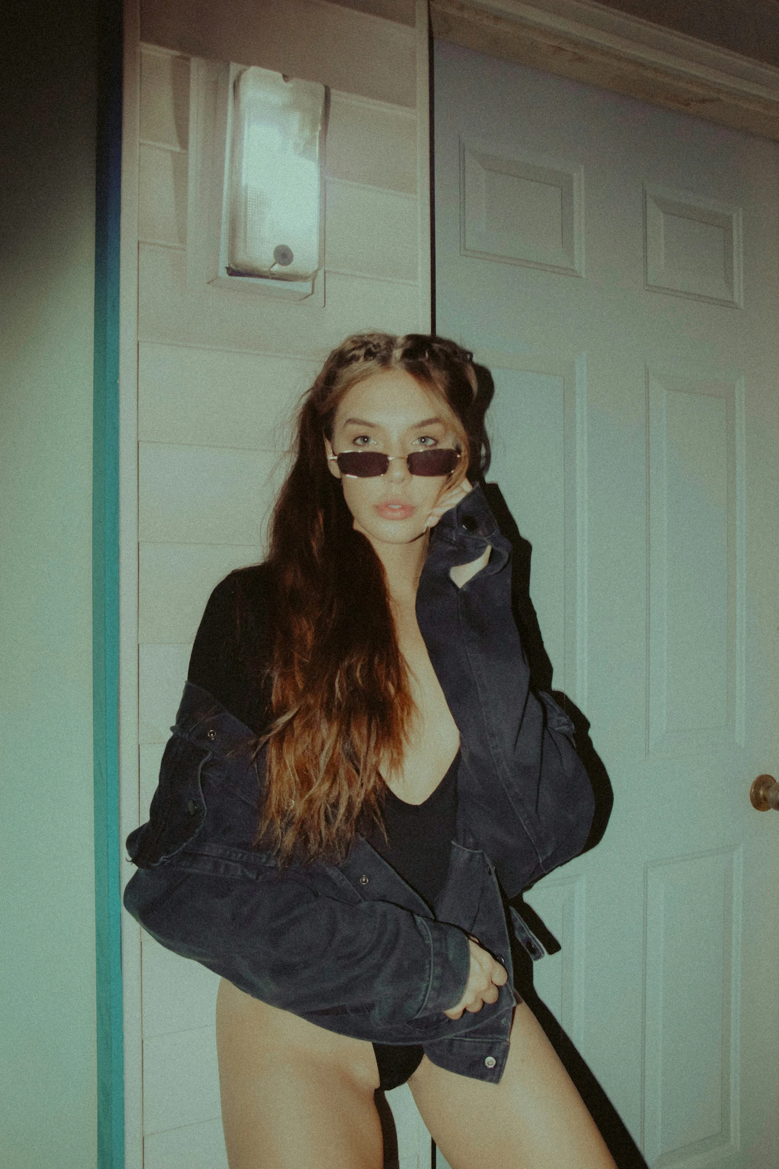 a woman in a leather jacket and sunglasses leaning against a wall