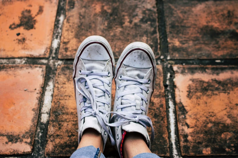 someone wearing white sneakers standing on top of an old brick road