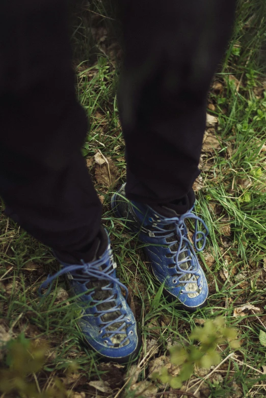 a person's feet in blue tennis shoes standing on green grass