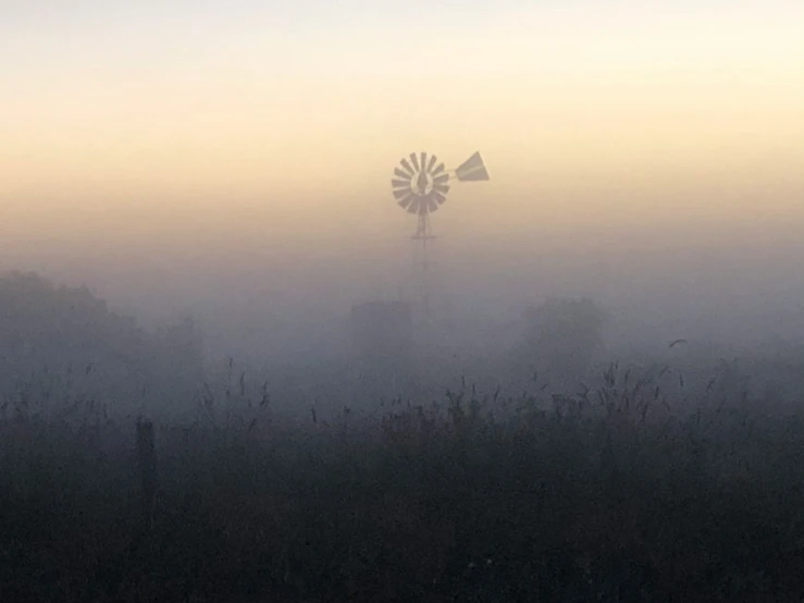 an old windmill sitting in the fog next to a field