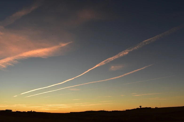 a silhouetted sunset shows contrails across the sky