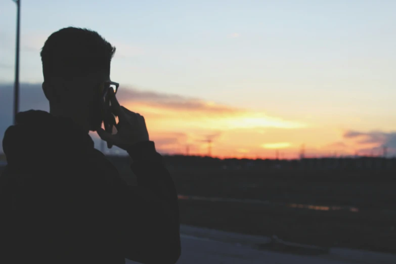 a man that is on his cellphone in front of a sunset