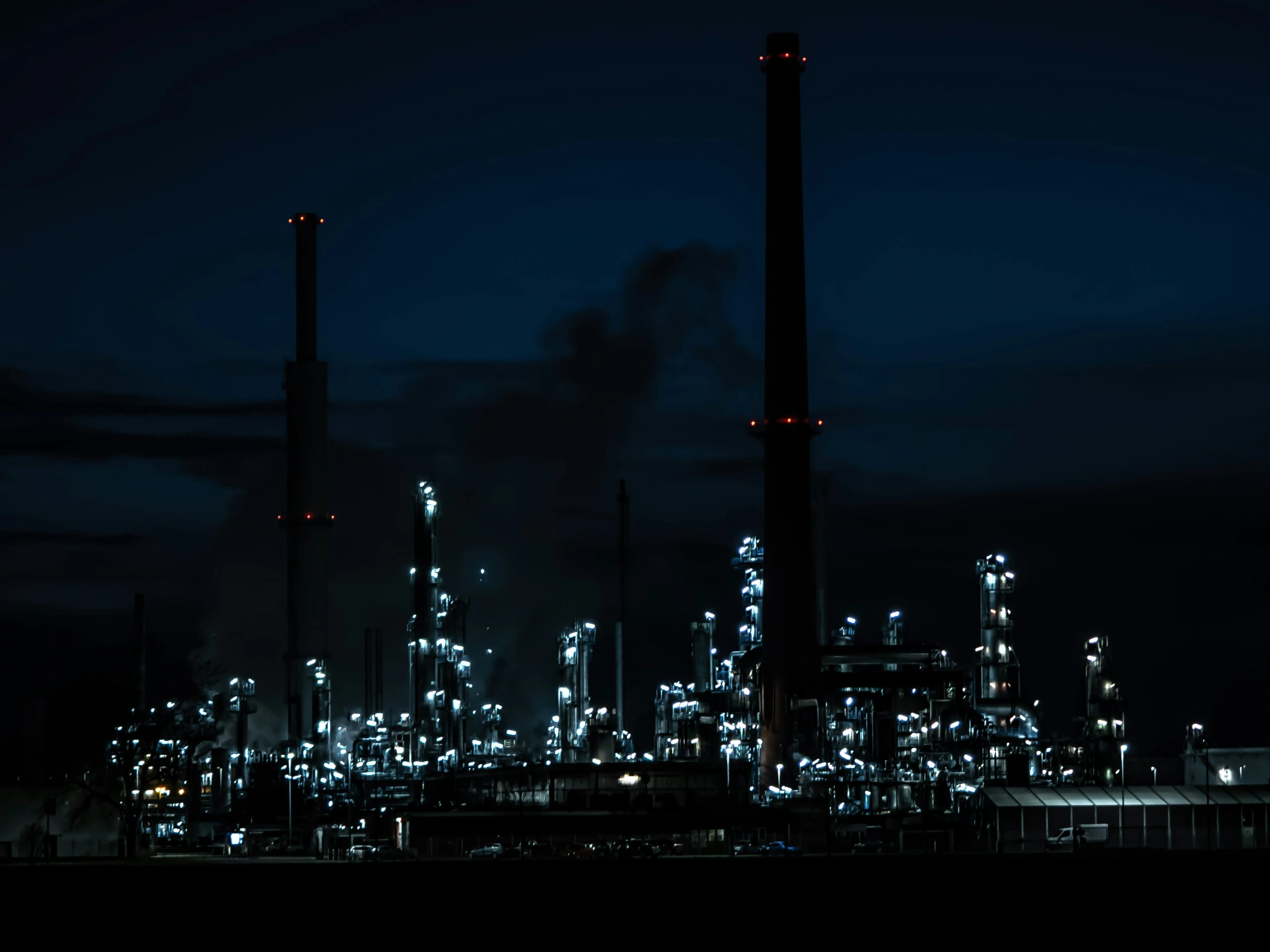 a dark night in a factory with smoke stacks and towers