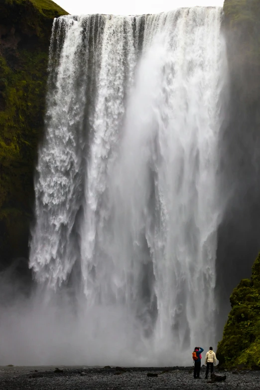 two people standing in front of a massive waterfall