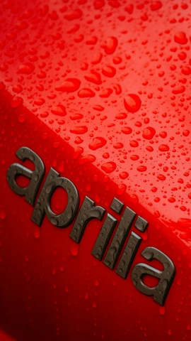 the back end of an all red car with a black emblem and water drops