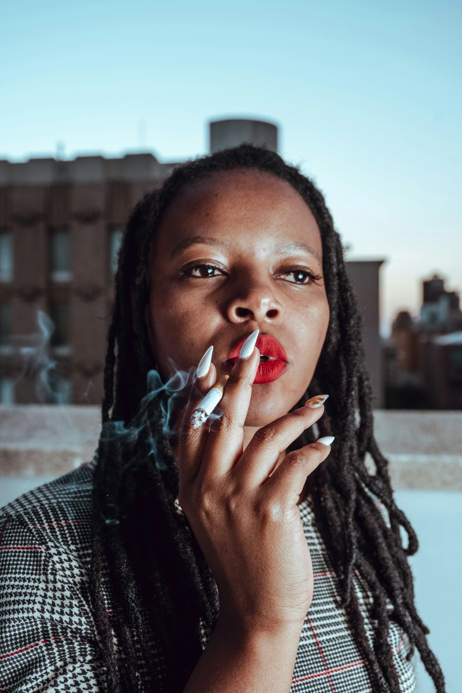 a woman with dread locks and manicured nails smoking a cigarette