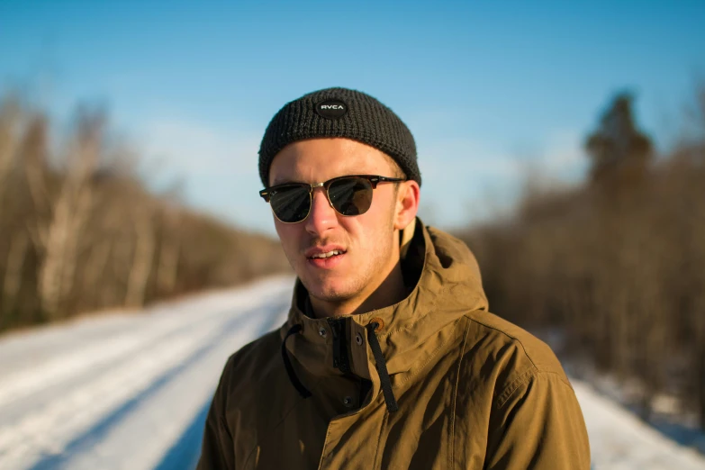 a man with shades and a hat on stands in the middle of a snowy road