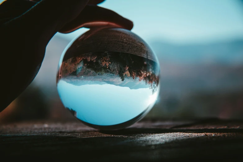 a hand holding a glass ball reflecting a mountain