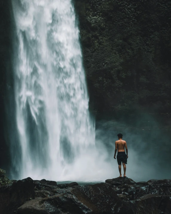 a man standing in front of a tall waterfall