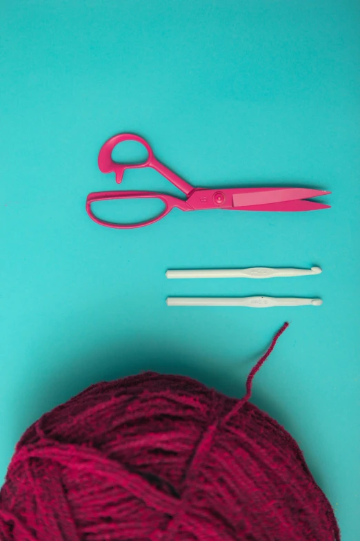 two pairs of crochet hooks and red yarn with pink scissors