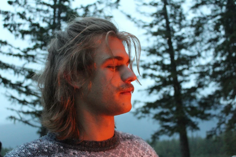 young man in warm sweater looking towards the trees