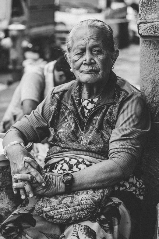 an old woman with a big smile sits against a pillar in the street