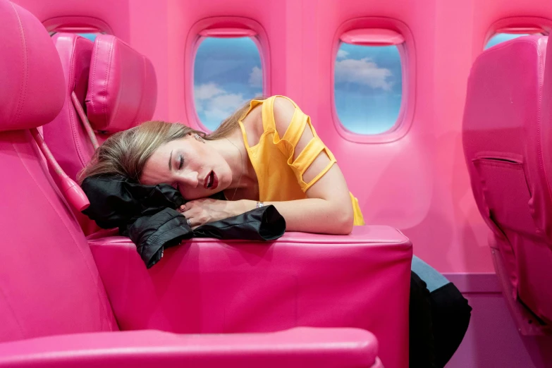 a beautiful young woman laying on top of a pink airplane seat