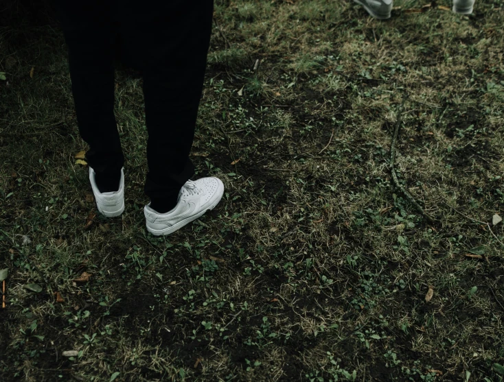 a person wearing white sneakers on top of some grass