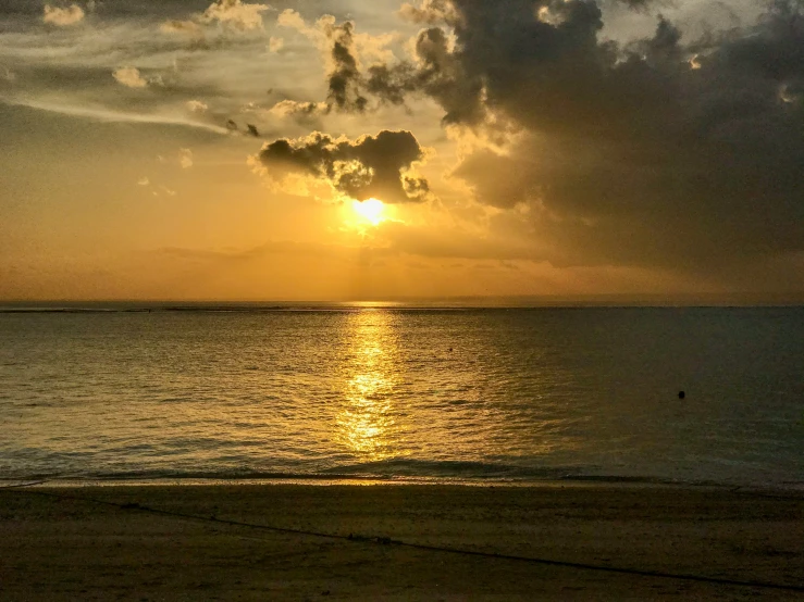 the sun setting over the ocean with a person on a beach