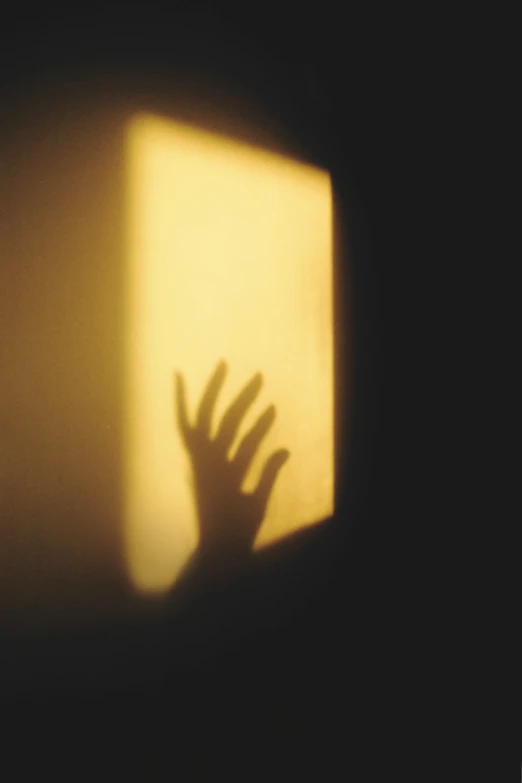 a shadow in the dark shows hand reaching up at a wall