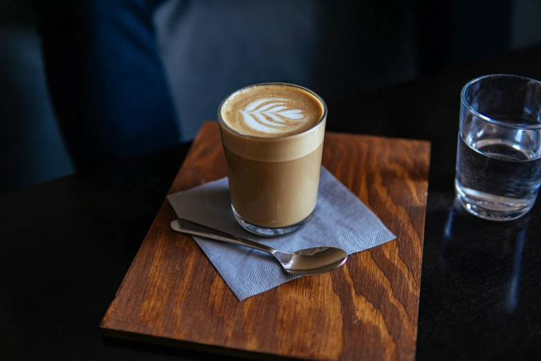 a cup of coffee on top of a wooden table next to a glass