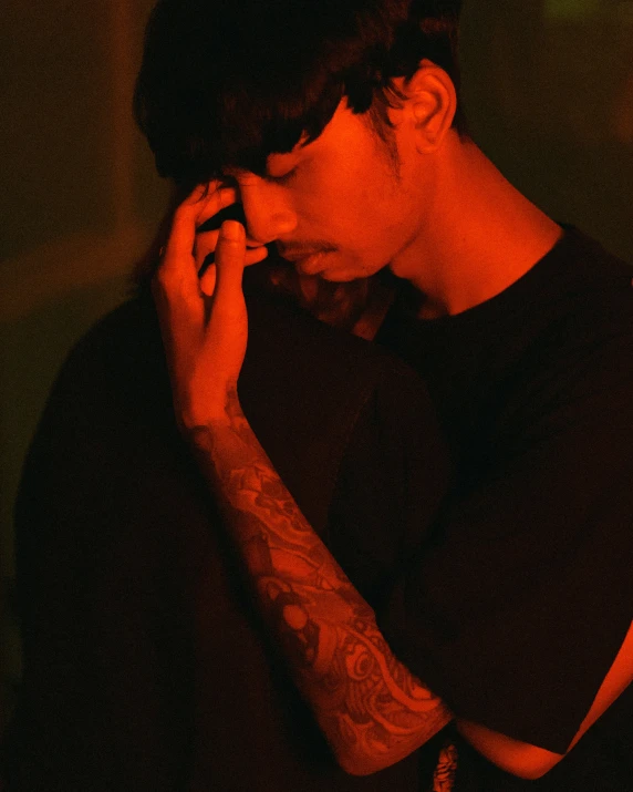 a young man holding his head in front of his hands while standing in the dark