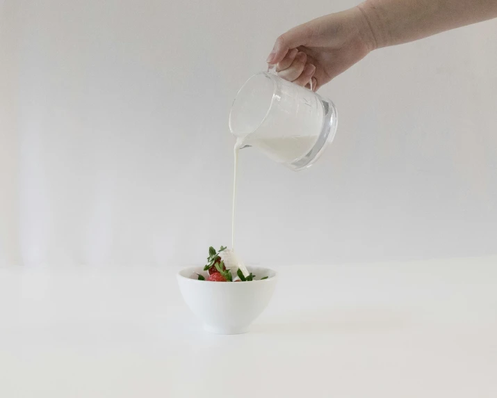 a white bowl containing a small salad and a hand drizzled in liquid