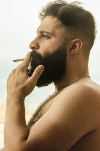 the man is smoking on the beach with his shirt off