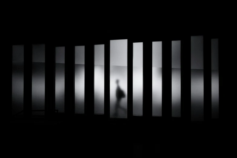 two people silhouetted against bars in an empty cell