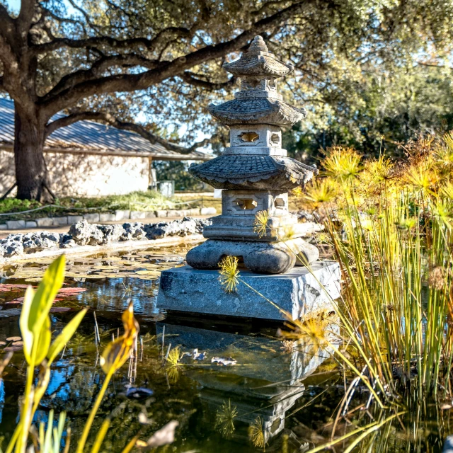 the statue stands near the water, in front of the house