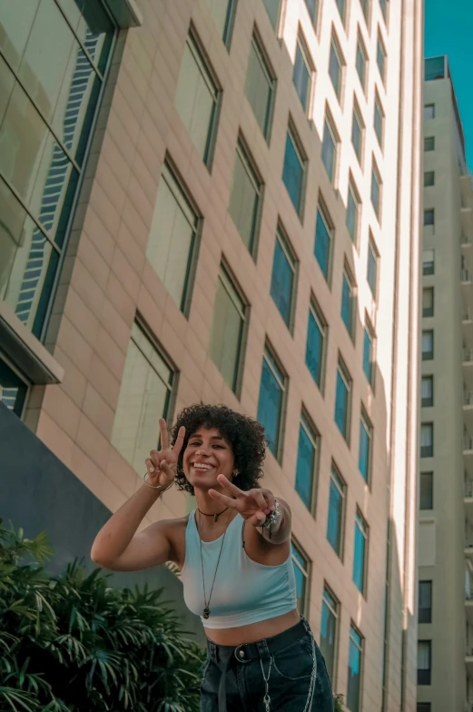 the woman is giving a peace sign as she stands on her skateboard in front of a tall building
