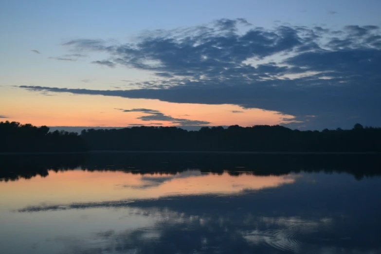 clouds, trees, and water reflect on the lake at sunset