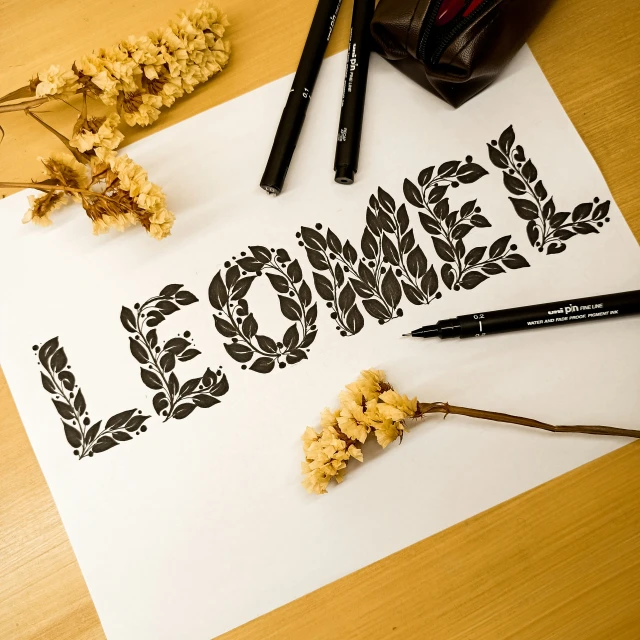 a table with a piece of white paper, flowers and pens