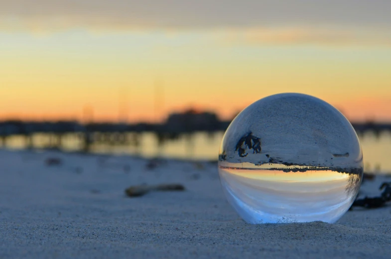 a crystal ball is on the sand with a beautiful sunset in the background