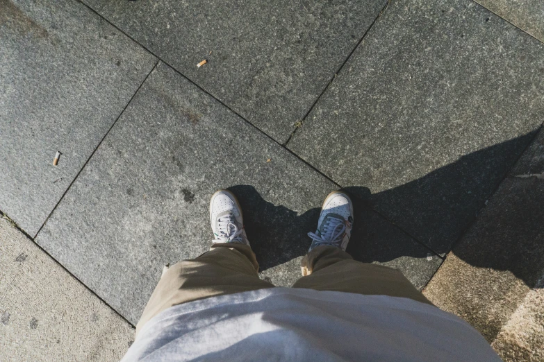 a person wearing white sneakers standing on a sidewalk