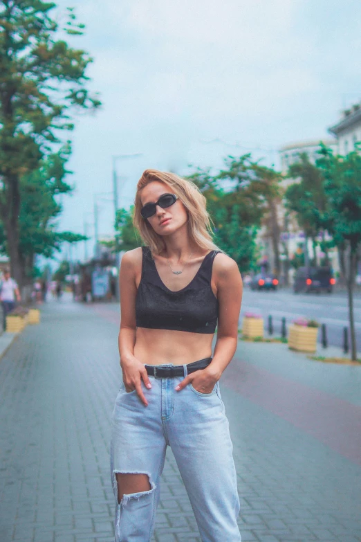 a young woman in a black tank top and jean pants stands on the street