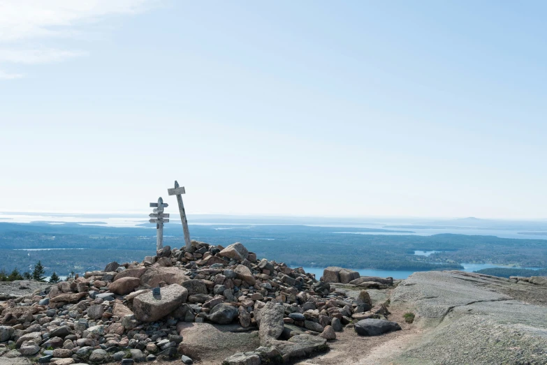 a mountain with rocks, a cross, and a lake in the background