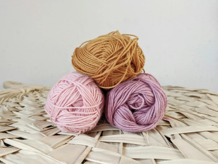 two balls of yarn sitting on a wicker surface