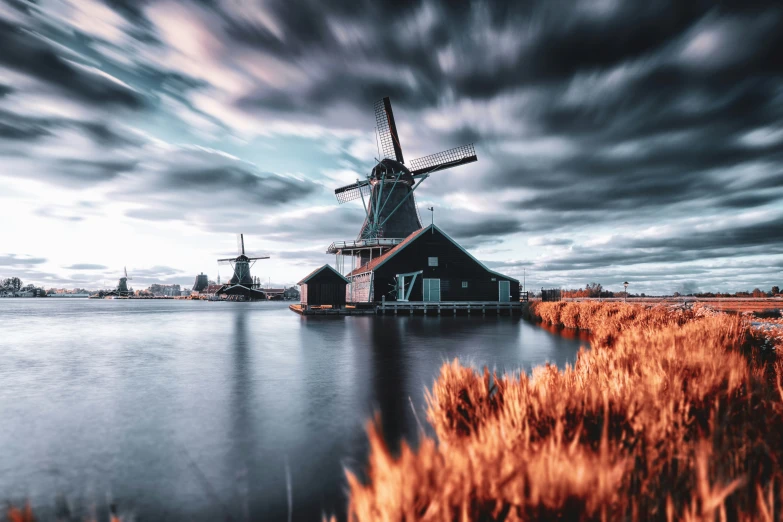 a windmill sits alone near a lake in the sunset