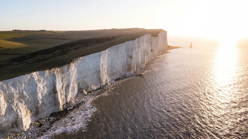 the sun rises over the cliffs in front of a person on a surfboard