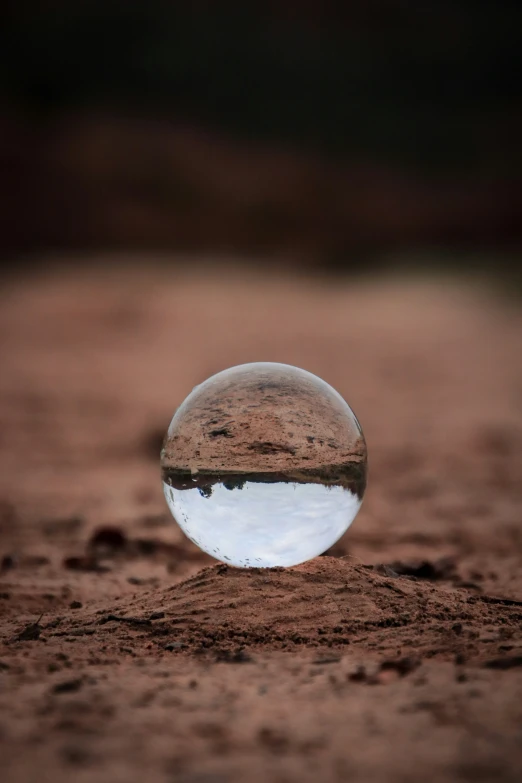 a sphere in the sand is reflecting a mountain