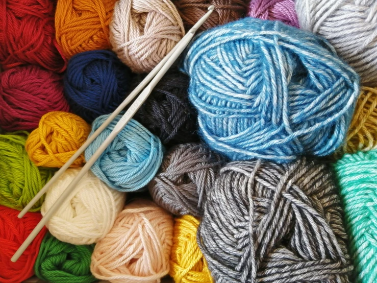 many colors of yarn and knitting needles on a wooden surface