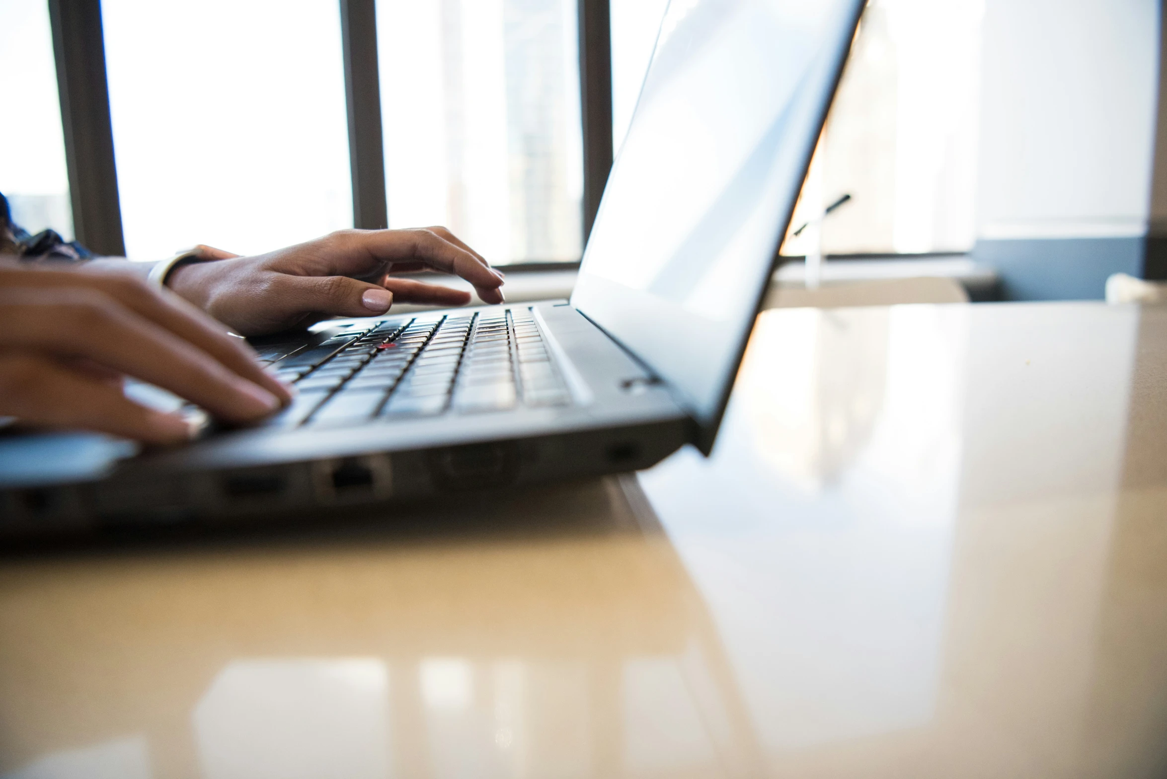 a person is sitting at a desk typing on their laptop