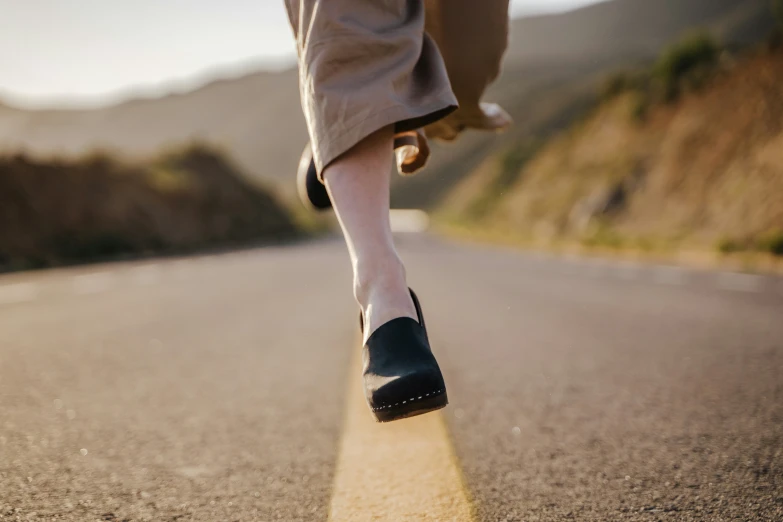 a person with a pair of shoes and long pants walking along the road