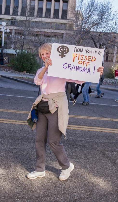 a woman walking down the road holding a sign with no you have picked grandma on it