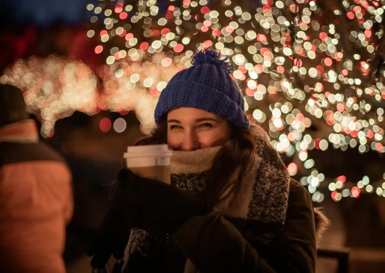 woman enjoying coffee outside, in front of a lit up tree