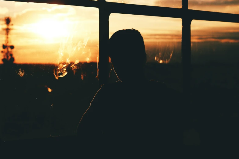 a silhouetted person looking out of a window at the sun setting