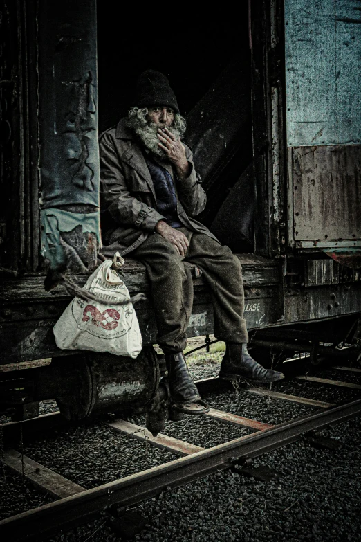 a man sitting on top of a wooden bench on a train track