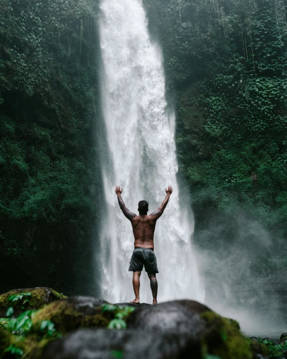 man standing in front of waterfall with hands in air