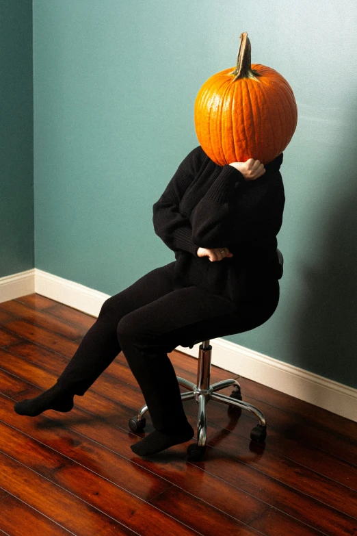 a person with a pumpkin head sitting in an office chair
