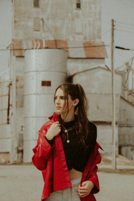 young woman standing in front of grain silos in red coat